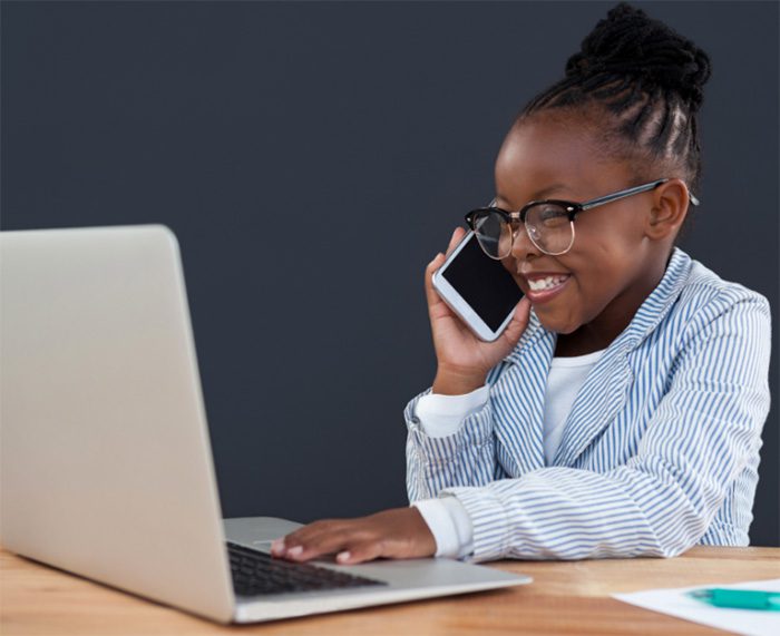 little girl looking at laptop and talking on phone while smiling